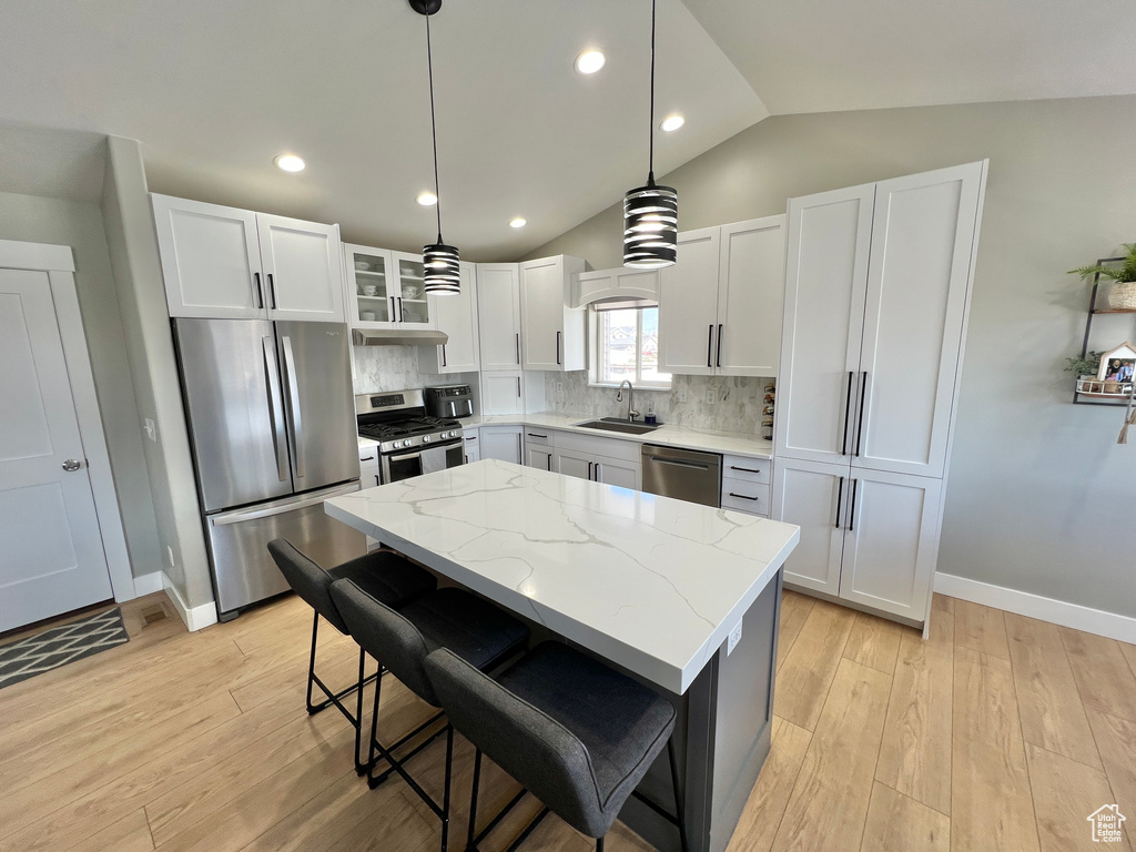 Kitchen featuring appliances with stainless steel finishes, backsplash, white cabinetry, decorative light fixtures, and vaulted ceiling