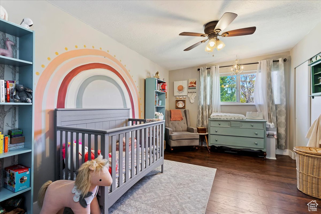 Bedroom featuring ceiling fan with notable chandelier, a nursery area, and dark wood-type flooring