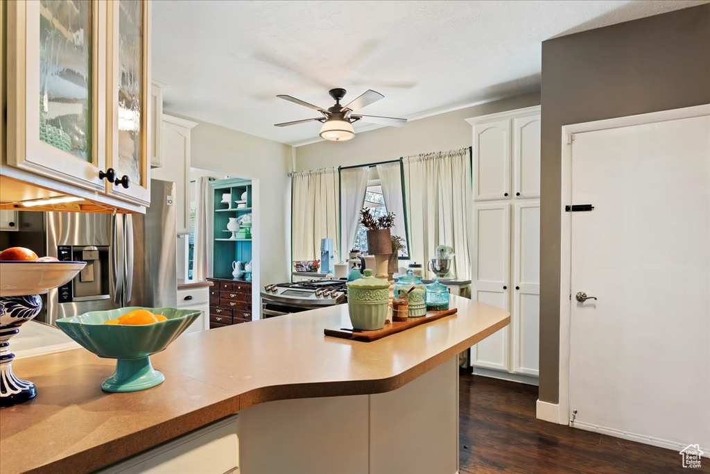 Kitchen featuring ceiling fan, white cabinets, dark hardwood / wood-style flooring, range with gas stovetop, and stainless steel fridge with ice dispenser