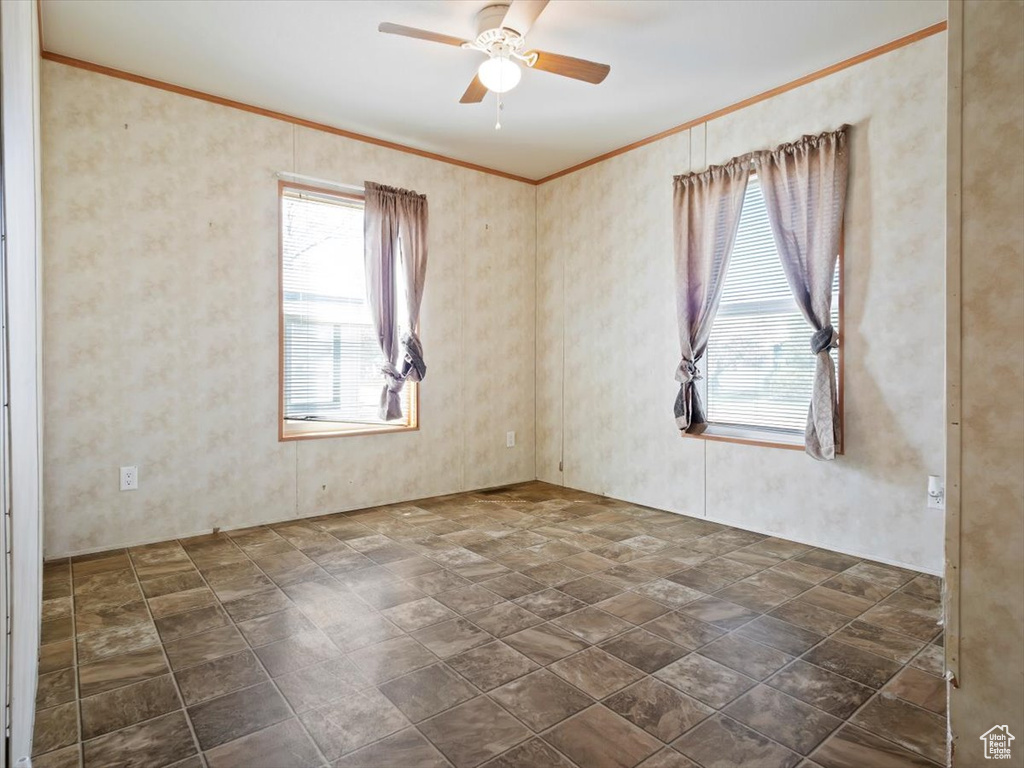 Tiled empty room featuring plenty of natural light, crown molding, and ceiling fan