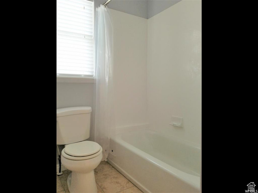 Bathroom featuring tile flooring, shower / tub combo, and toilet