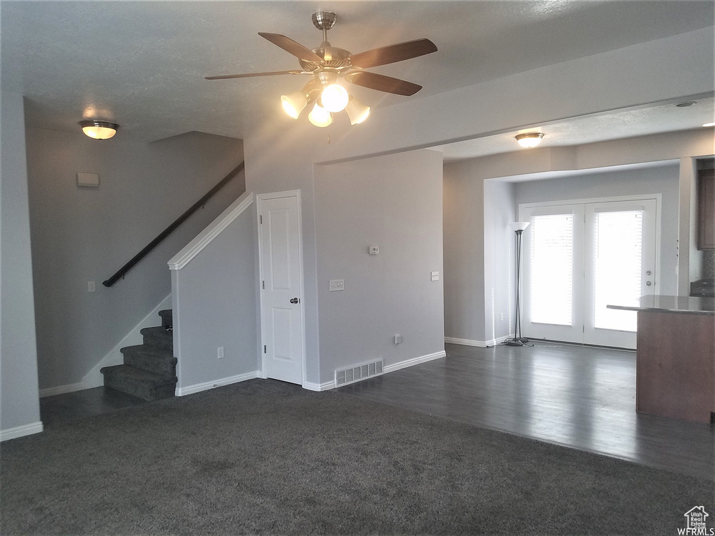 Unfurnished living room featuring ceiling fan, french doors, and dark colored carpet