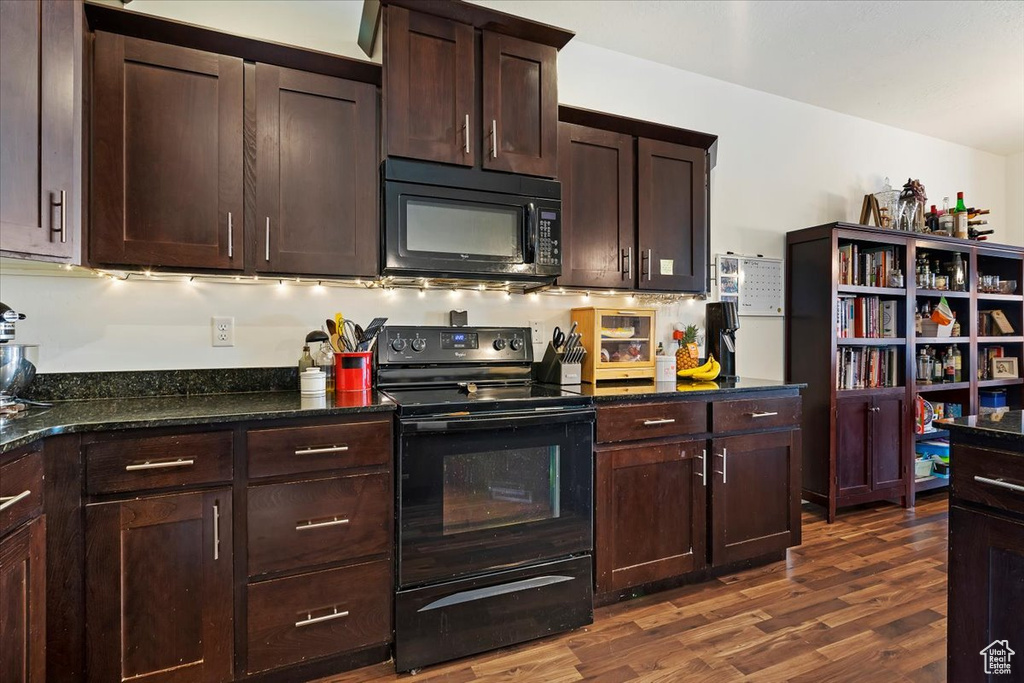 Kitchen with dark stone counters, dark brown cabinetry, black appliances, and dark hardwood / wood-style flooring