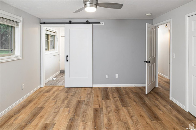 Unfurnished bedroom featuring ceiling fan, hardwood / wood-style flooring, and a barn door
