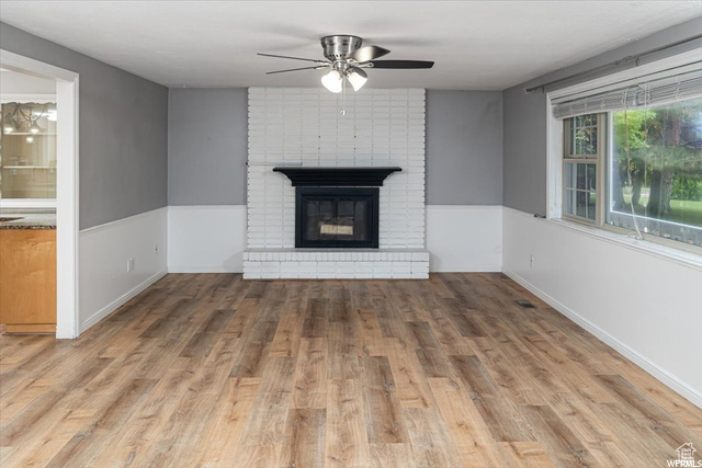 Unfurnished living room with brick wall, a fireplace, ceiling fan, and hardwood / wood-style flooring
