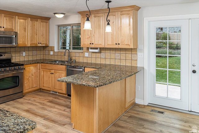 Kitchen with dark stone countertops, plenty of natural light, pendant lighting, and stainless steel appliances