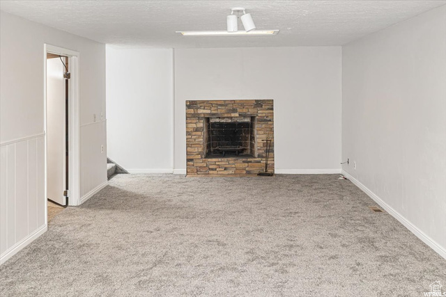 Unfurnished living room with light carpet, a stone fireplace, and a textured ceiling
