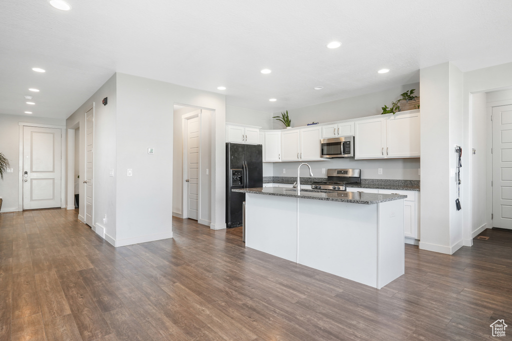Kitchen featuring appliances with stainless steel finishes, white cabinets, a kitchen island with sink, dark stone countertops, and dark hardwood / wood-style flooring