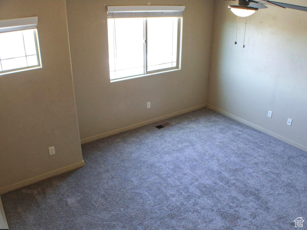 Unfurnished room with ceiling fan, a wealth of natural light, and dark colored carpet