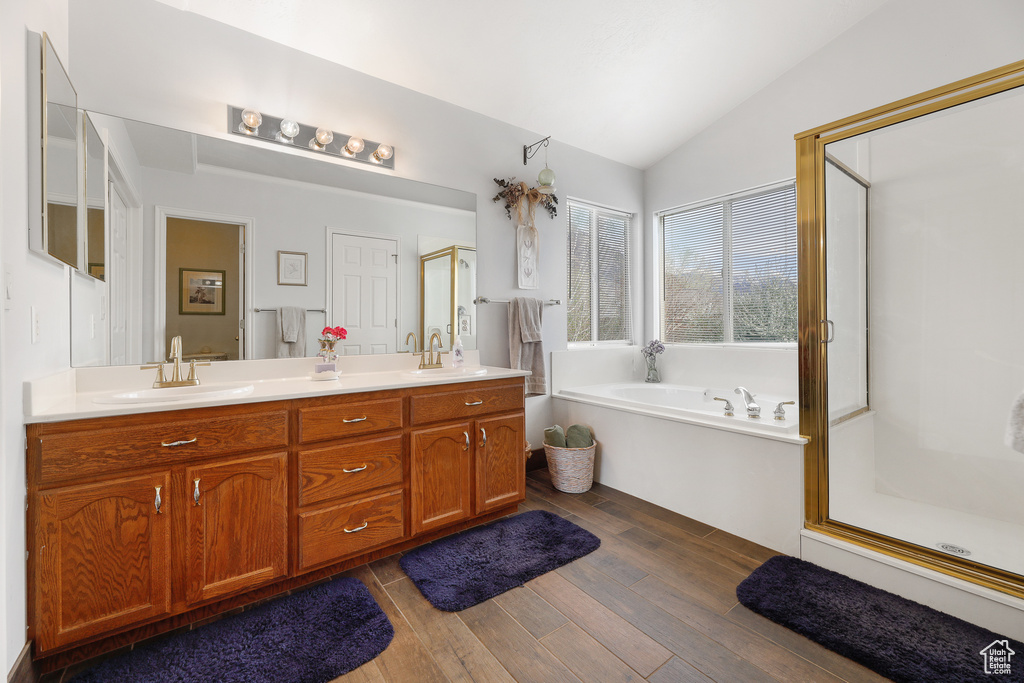 Bathroom with wood-type flooring, separate shower and tub, large vanity, dual sinks, and lofted ceiling