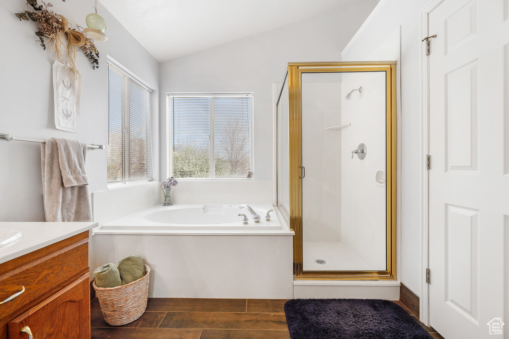 Bathroom with wood-type flooring, shower with separate bathtub, vanity, and lofted ceiling