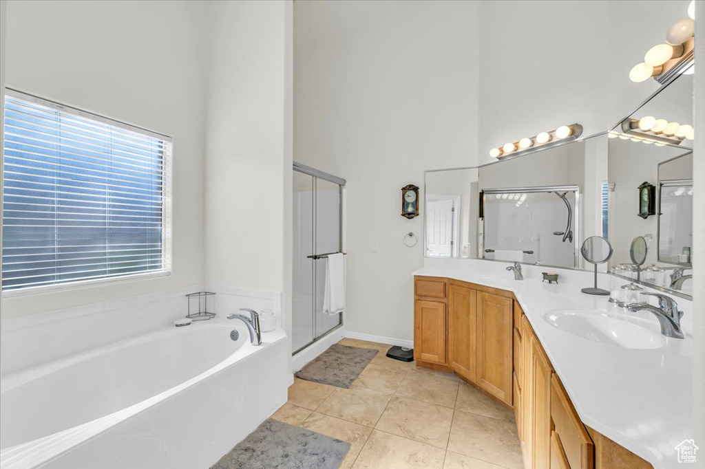 Bathroom featuring dual sinks, a towering ceiling, shower with separate bathtub, vanity with extensive cabinet space, and tile floors