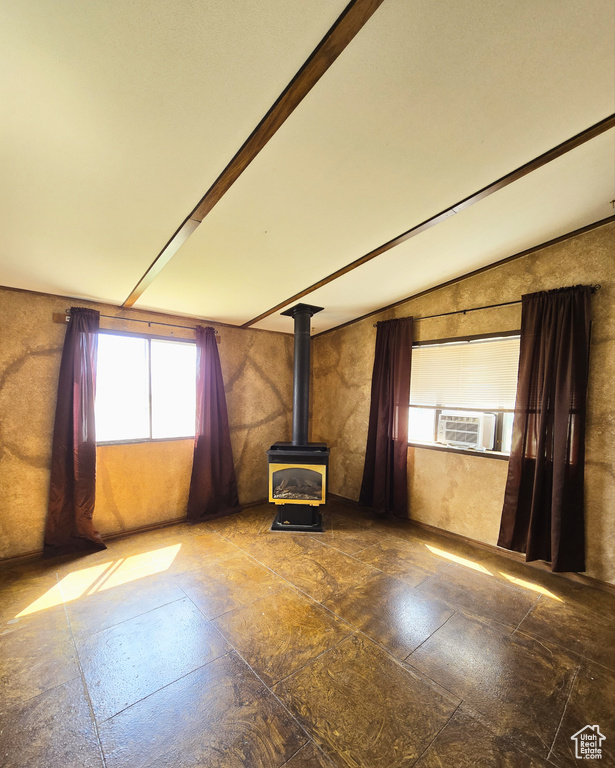 Unfurnished living room featuring lofted ceiling with beams, dark tile flooring, and a wood stove