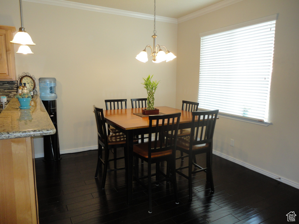 Dining area featuring a notable chandelier, plenty of natural light, crown molding, and dark wood-type flooring