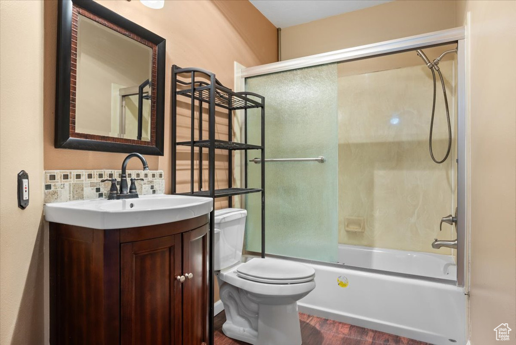 Full bathroom featuring vanity, hardwood / wood-style floors, backsplash, combined bath / shower with glass door, and toilet