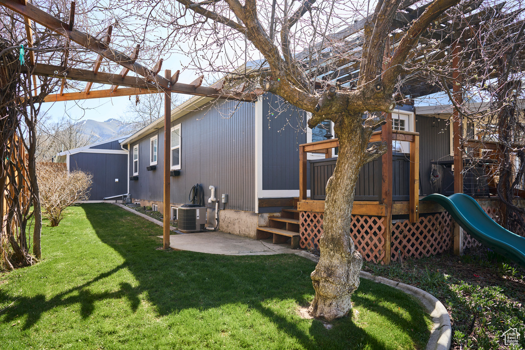 Rear view of house with a playground, a deck with mountain view, central AC unit, and a lawn
