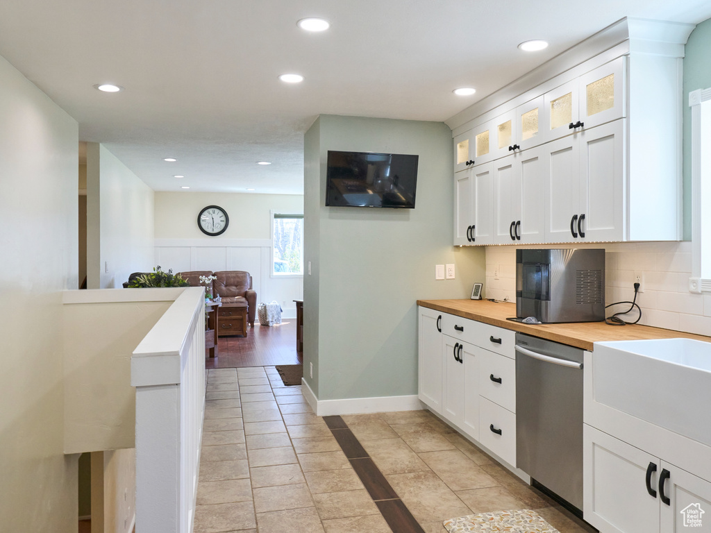 Kitchen featuring white cabinets, backsplash, light tile floors, and stainless steel dishwasher