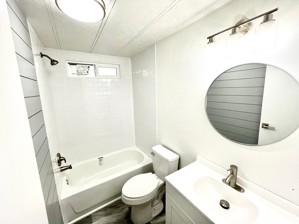 Full bathroom with tiled shower / bath combo, a textured ceiling, vanity, and toilet