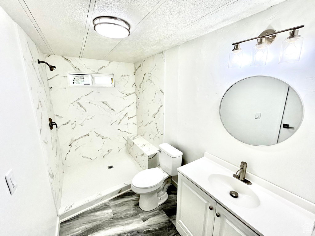 Bathroom with a textured ceiling, vanity, toilet, and a tile shower