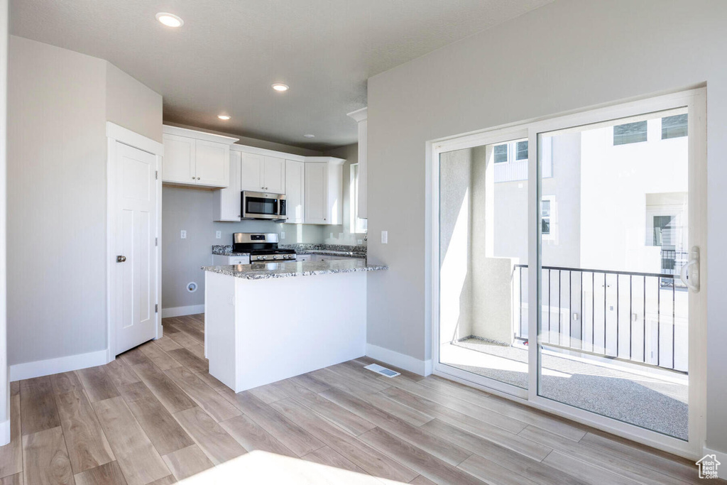Kitchen featuring kitchen peninsula, light hardwood / wood-style floors, range, light stone counters, and white cabinets