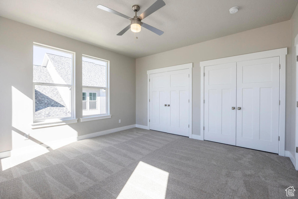 Unfurnished bedroom with light carpet, ceiling fan, and multiple closets