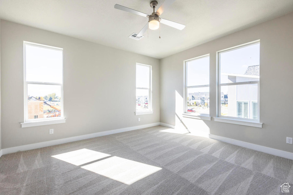 Carpeted spare room featuring a wealth of natural light and ceiling fan