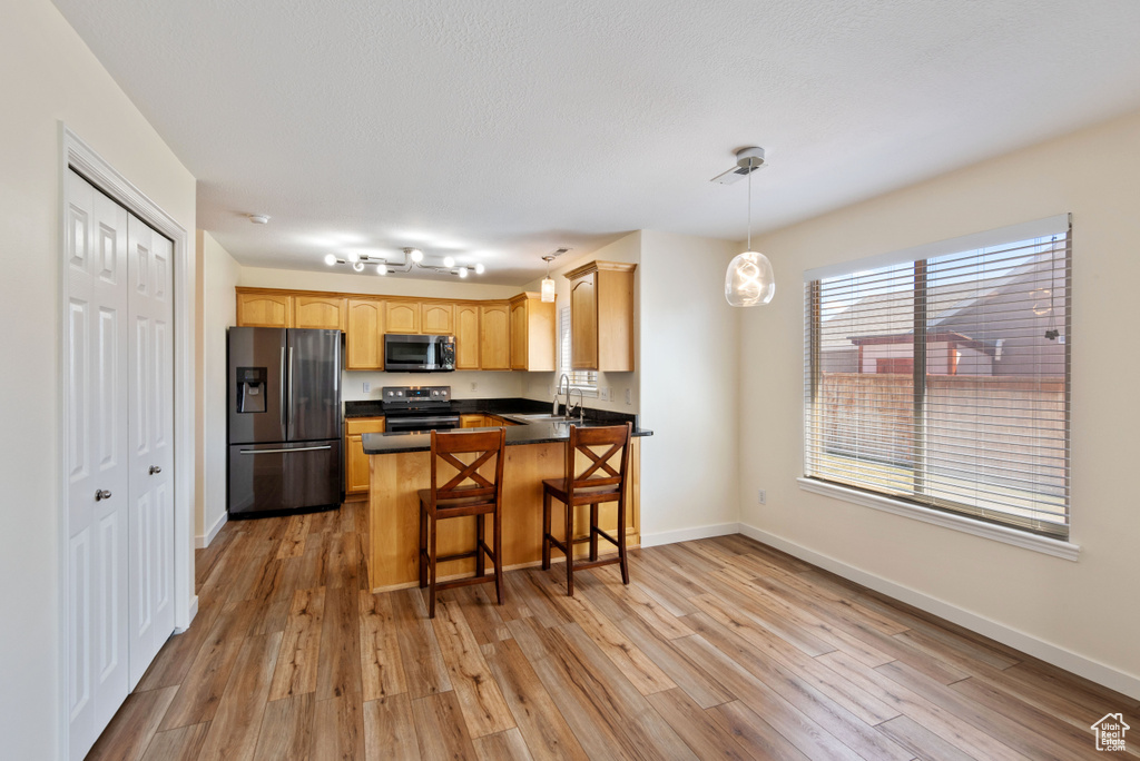 Kitchen featuring appliances with stainless steel finishes, light hardwood / wood-style flooring, pendant lighting, and a breakfast bar