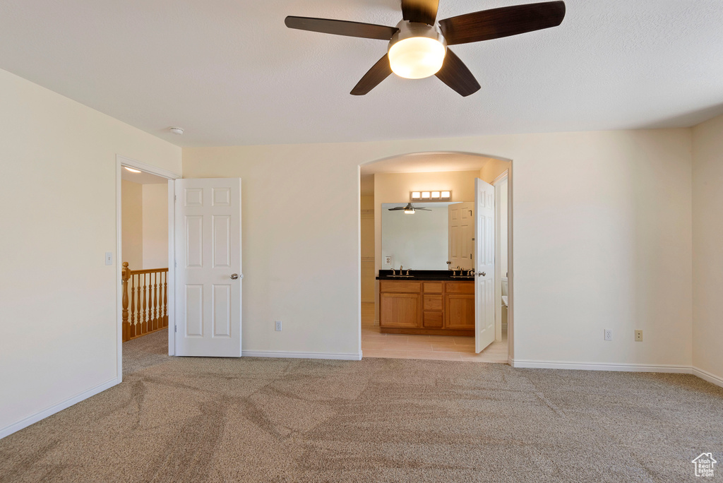 Unfurnished bedroom with light colored carpet, sink, ceiling fan, and ensuite bathroom