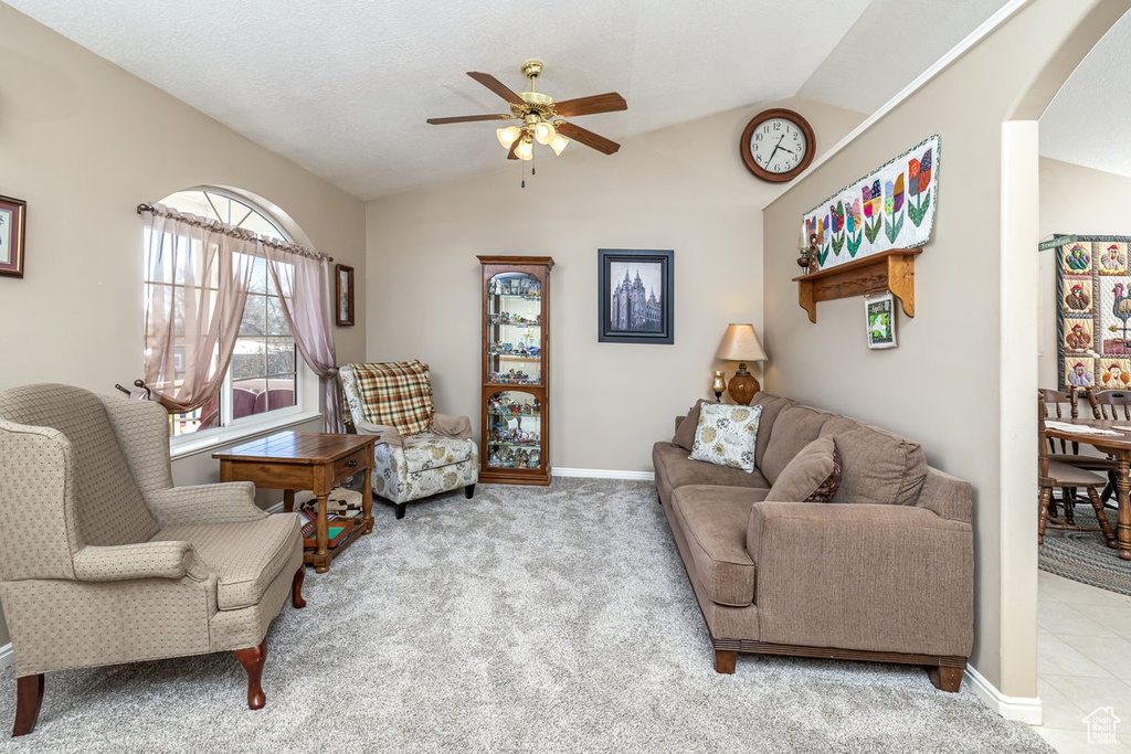 Living room featuring light colored carpet, vaulted ceiling, ceiling fan, and a textured ceiling