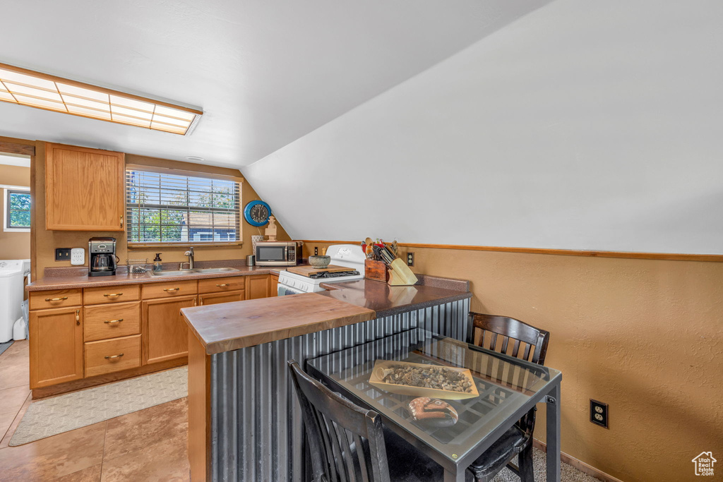 Kitchen with gas stove, a kitchen breakfast bar, sink, vaulted ceiling, and light tile floors