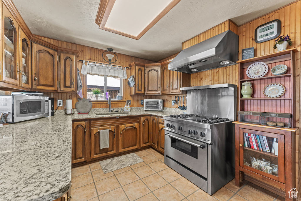 Kitchen with sink, wall chimney exhaust hood, stainless steel appliances, and light tile floors