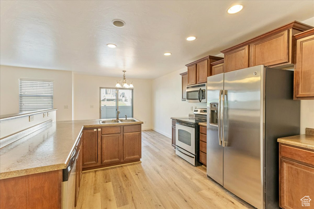Kitchen with appliances with stainless steel finishes, light hardwood / wood-style flooring, sink, and hanging light fixtures