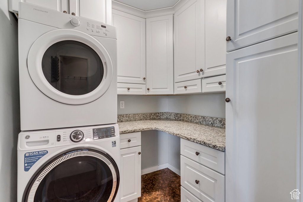 Laundry area with stacked washer and clothes dryer, dark tile flooring, and cabinets