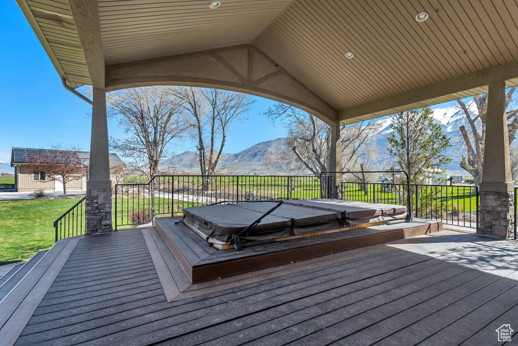 Wooden deck with a mountain view, a covered hot tub, and a lawn