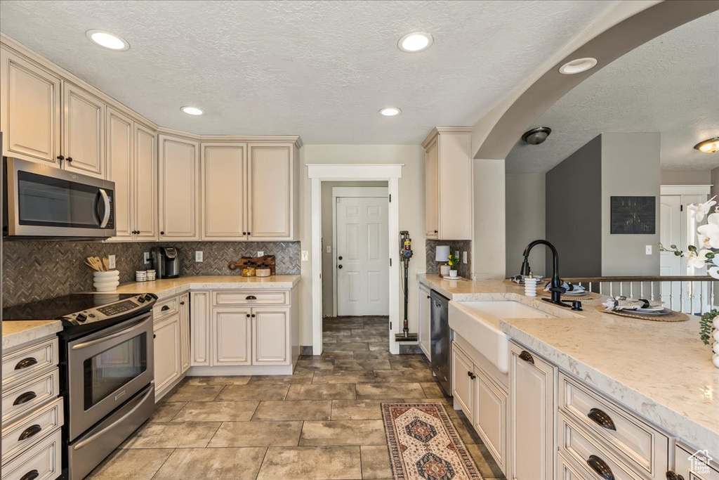 Kitchen with tasteful backsplash, stainless steel appliances, light tile floors, sink, and cream cabinetry