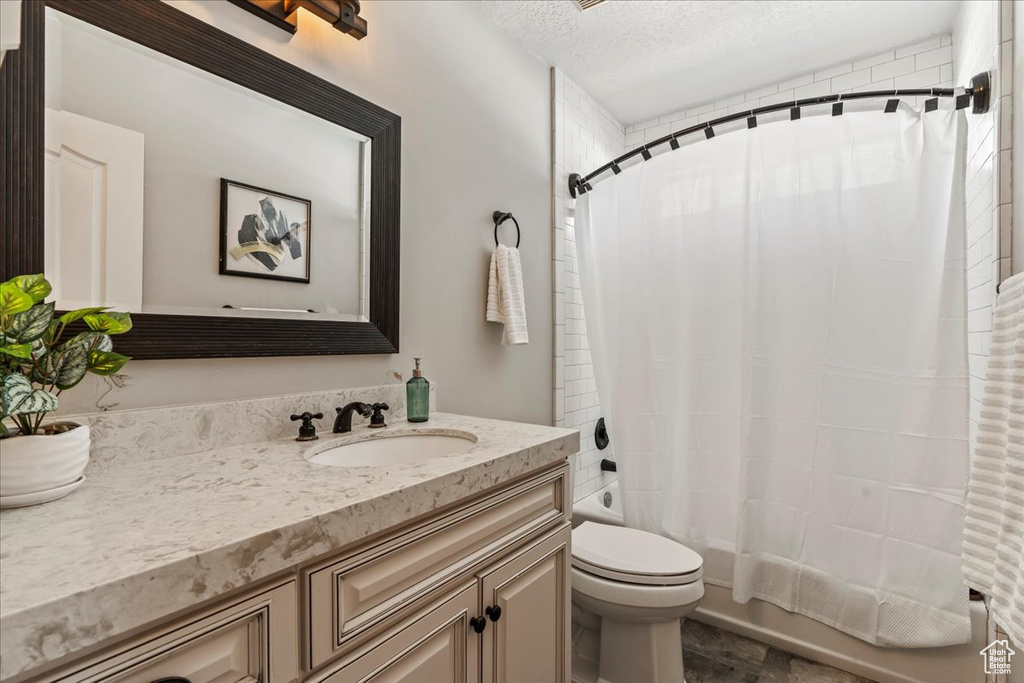 Full bathroom featuring shower / tub combo, tile floors, vanity, toilet, and a textured ceiling