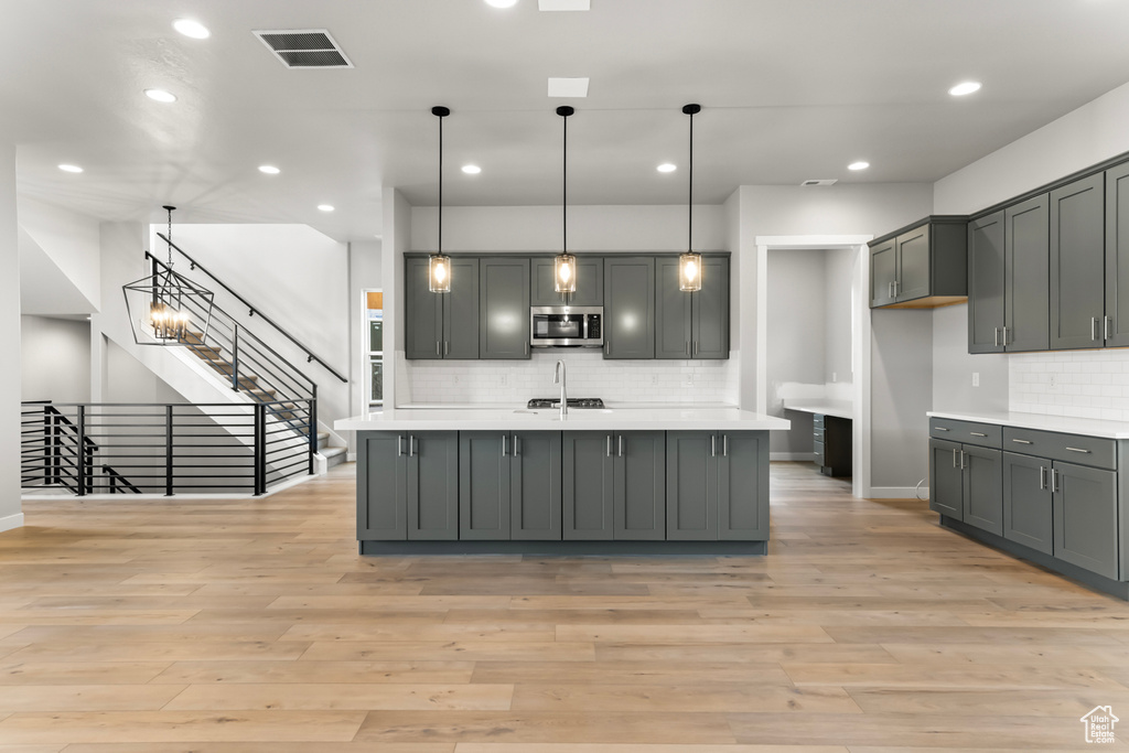 Kitchen featuring a kitchen island with sink, decorative light fixtures, light hardwood / wood-style flooring, gray cabinets, and backsplash