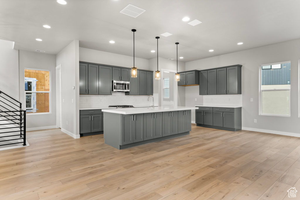 Kitchen with pendant lighting, a kitchen island with sink, light wood-type flooring, gray cabinetry, and tasteful backsplash