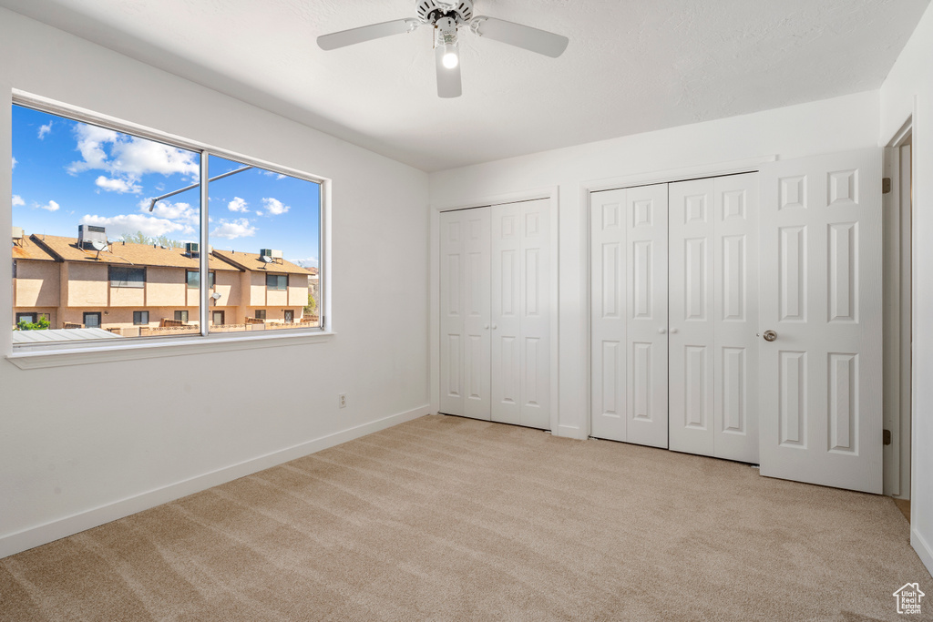 Unfurnished bedroom with light carpet, ceiling fan, and two closets