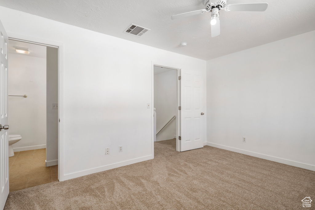 Unfurnished bedroom featuring ceiling fan, light colored carpet, and ensuite bath