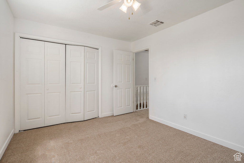 Unfurnished bedroom with ceiling fan, light carpet, and a closet