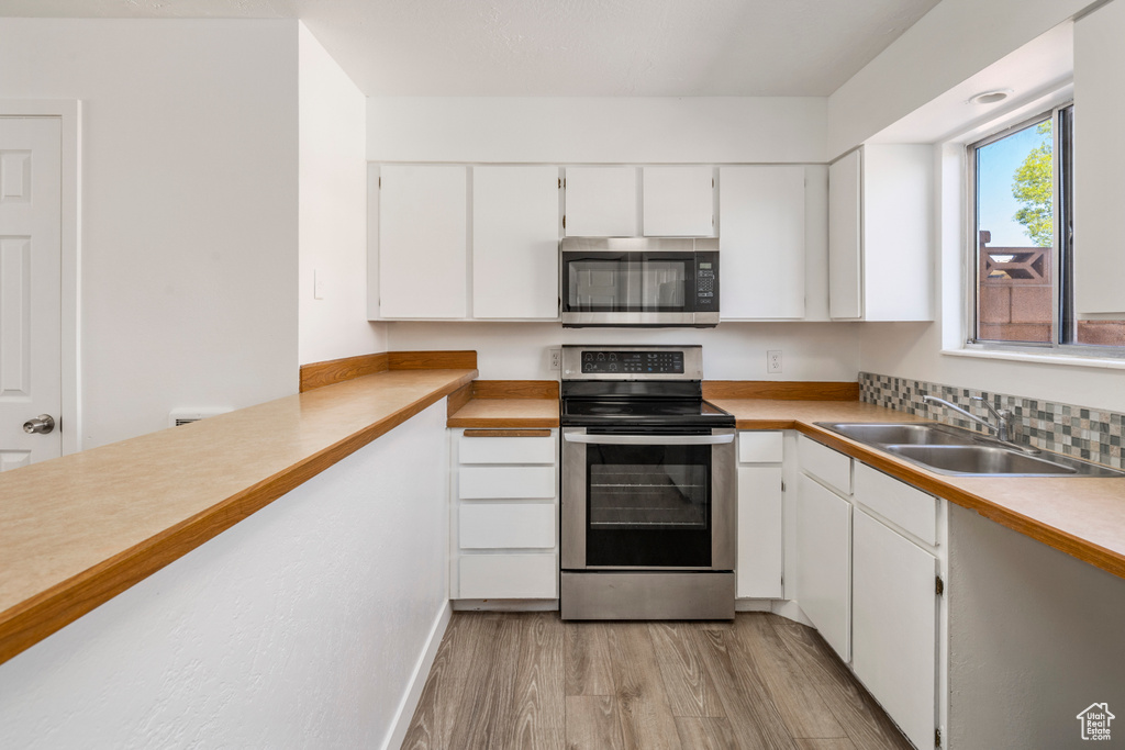 Kitchen with appliances with stainless steel finishes, light hardwood / wood-style floors, white cabinetry, and sink