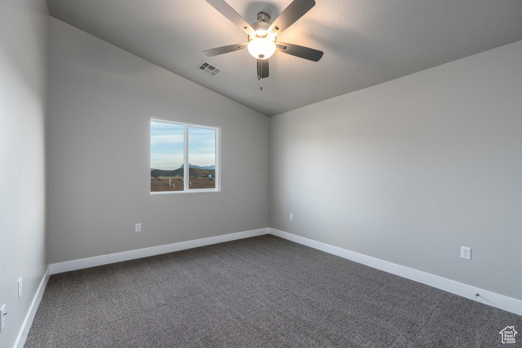 Empty room with vaulted ceiling, ceiling fan, and dark carpet