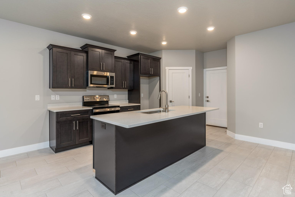 Kitchen featuring dark brown cabinetry, sink, appliances with stainless steel finishes, and an island with sink