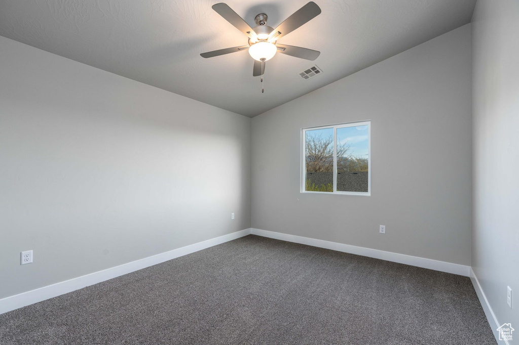 Spare room featuring dark carpet, ceiling fan, and lofted ceiling