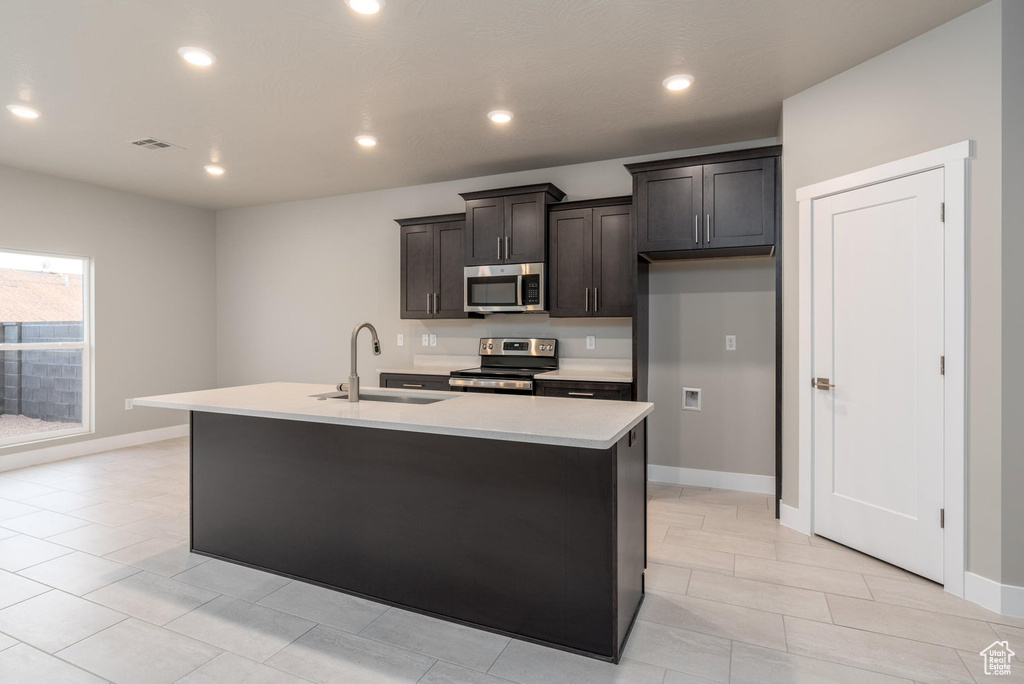 Kitchen featuring a kitchen island with sink, stainless steel appliances, sink, and light tile flooring