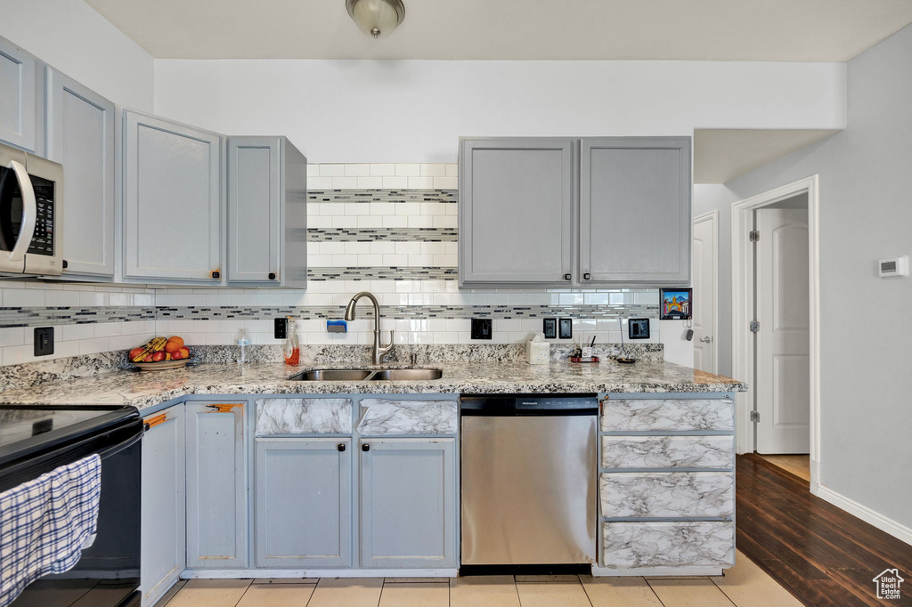 Kitchen featuring sink, light hardwood / wood-style floors, dishwasher, tasteful backsplash, and light stone countertops