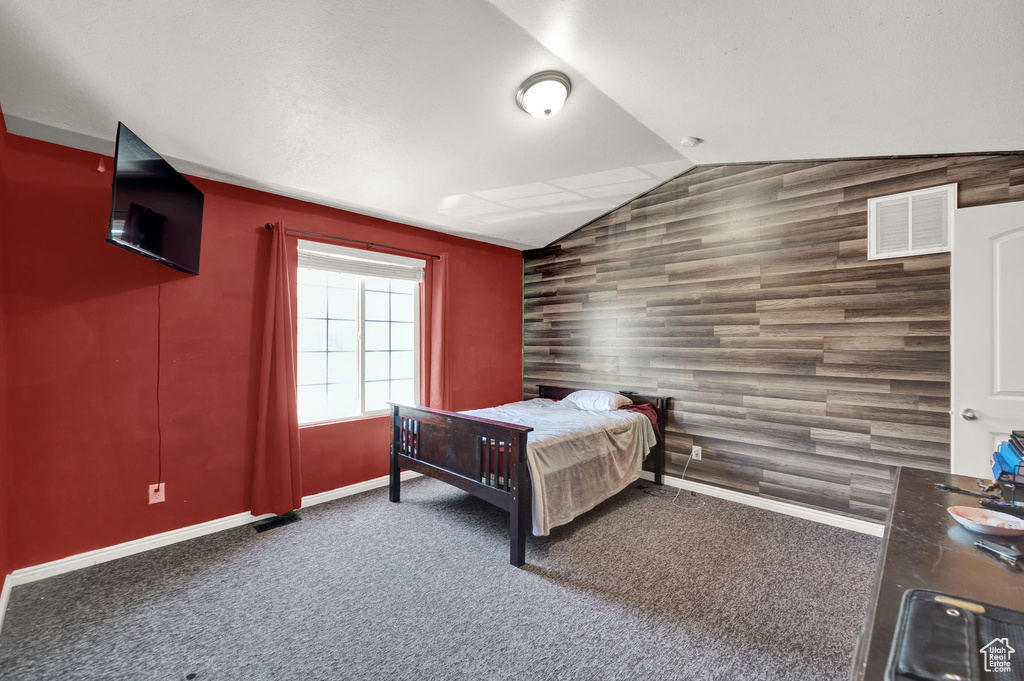 Bedroom with lofted ceiling, wood walls, and dark colored carpet