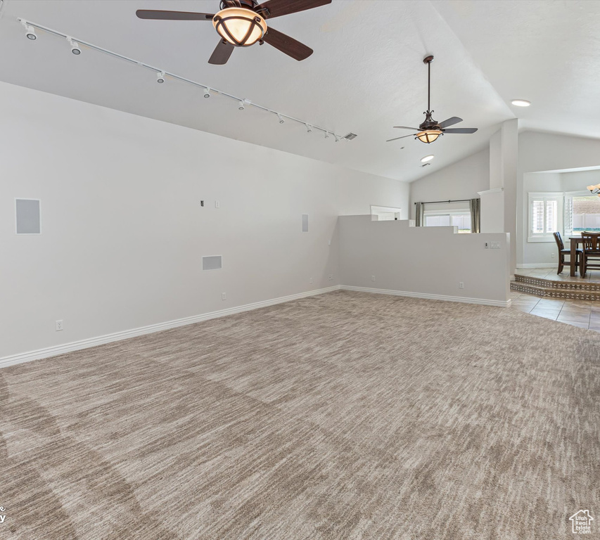Unfurnished living room featuring rail lighting, light colored carpet, ceiling fan, and lofted ceiling