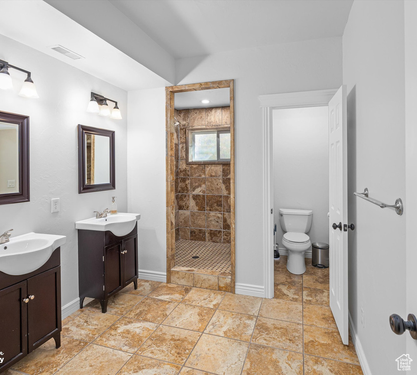 Bathroom featuring tile flooring, a tile shower, toilet, and dual bowl vanity